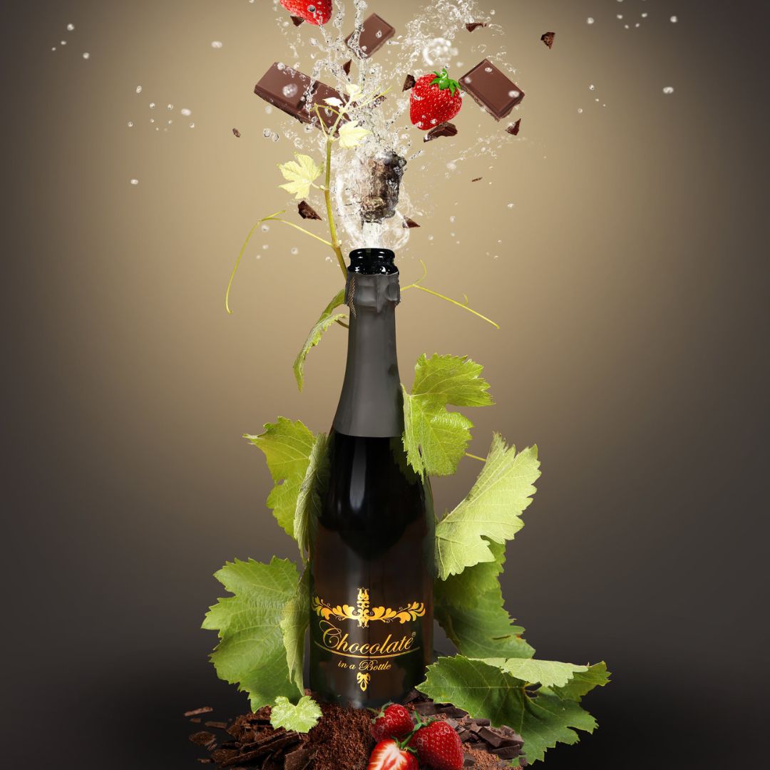 Flasche alkoholfreie Sekt-Alternative umgeben von Schokoladenstücken, Erdbeeren und Weinblättern