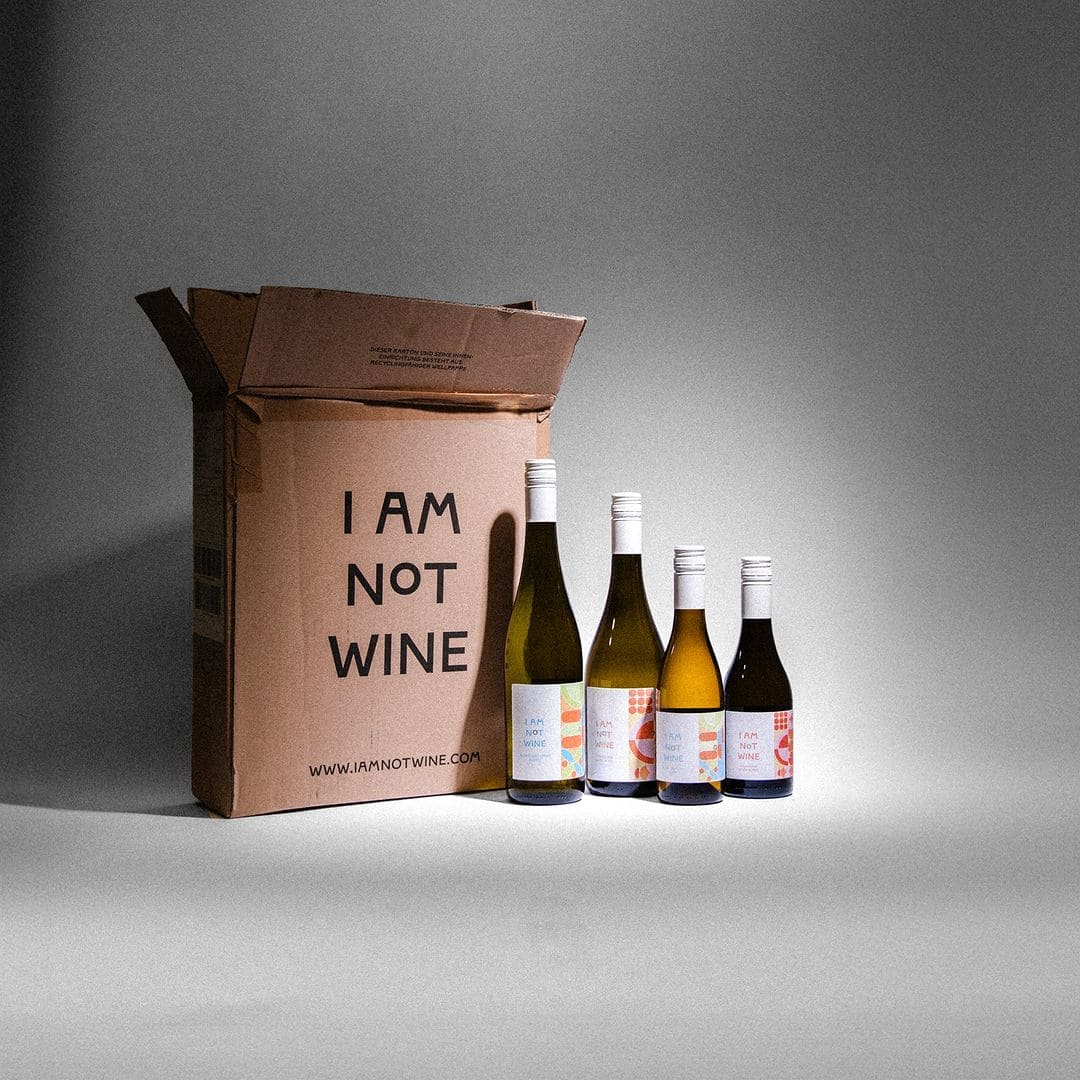 Vier Flaschen alkoholfreier Wein von 'I Am Not Wine' neben einer offenen Versandbox