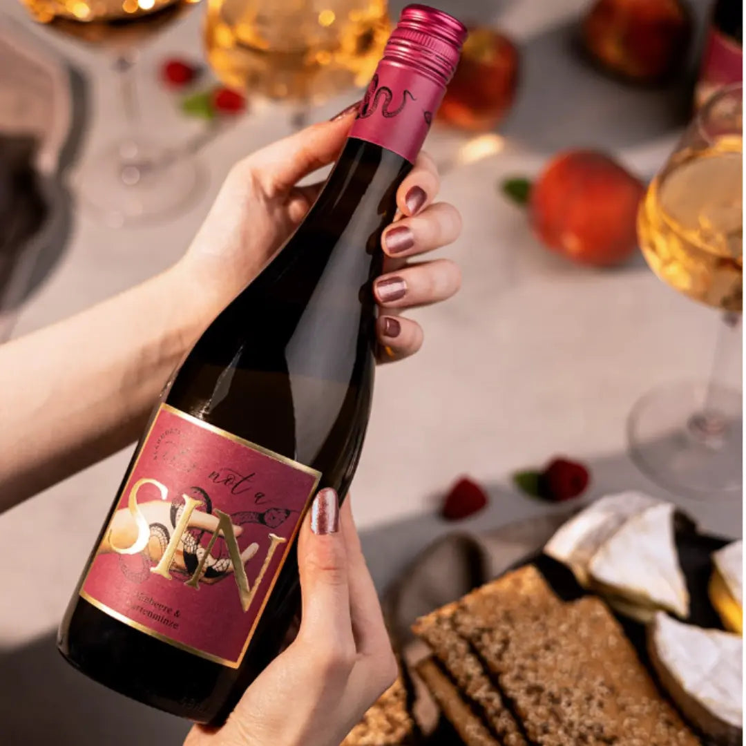 Alkoholfreier Rosé-Sekt „It’s not a SIN“ in der Hand, stilvoll inszeniert mit Gläsern, Erdbeeren und Snacks auf festlich gedecktem Tisch.